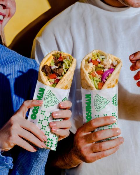 Two people holding freshly made Lebanese wraps filled with salad and grilled ingredients