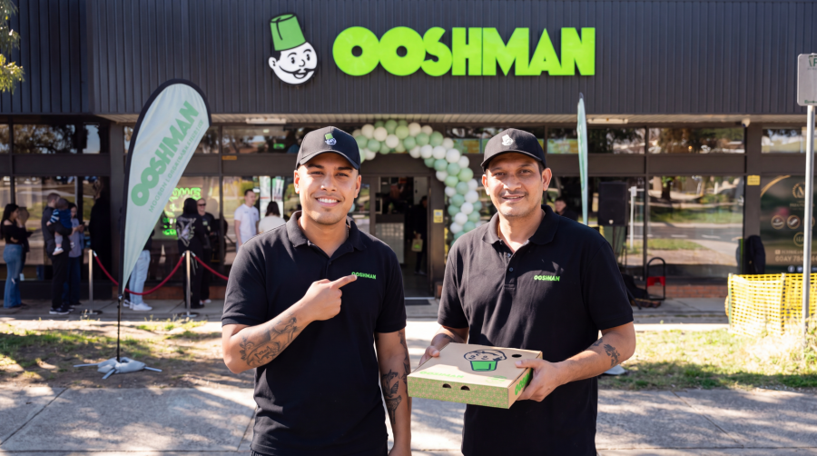 Two OOSHMAN team members smiling outside a store, one holding a pizza box