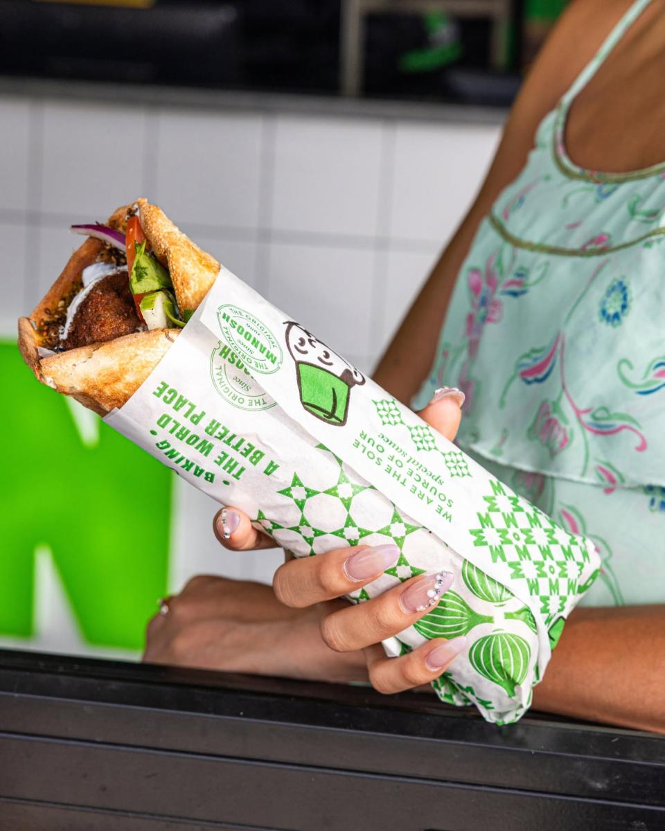 Person holding a fresh OOSHMAN Lebanese wrap in branded takeaway packaging