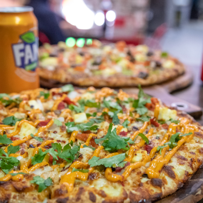 Two freshly baked loaded pizzas with herbs and sauce, served beside an orange soft drink