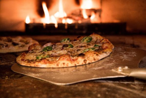 Freshly baked cheese pizza with herbs on a peel beside a wood-fired oven