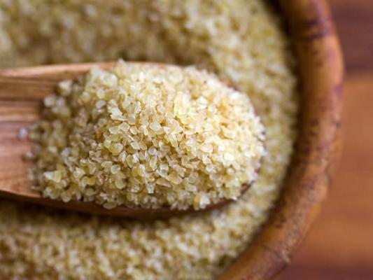 Wooden spoon filled with coarse bulgur wheat over a bowl of grains