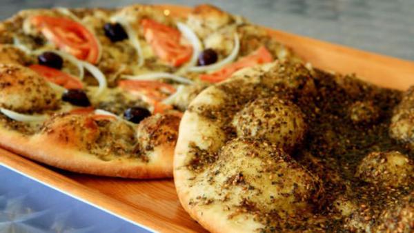 Two freshly baked Lebanese manoosh flatbreads, including zaatar and vegetable toppings