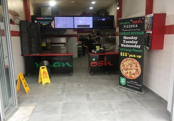 Entrance to a Manoosh pizzeria with menu screens, counter and pizza deal sign