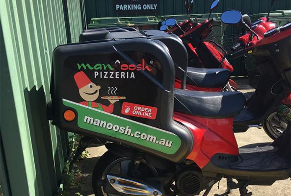 Red Manoosh Pizzeria delivery scooter parked beside other motorbikes