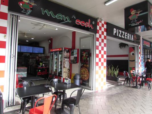 Manoosh pizzeria storefront with outdoor tables and red chairs