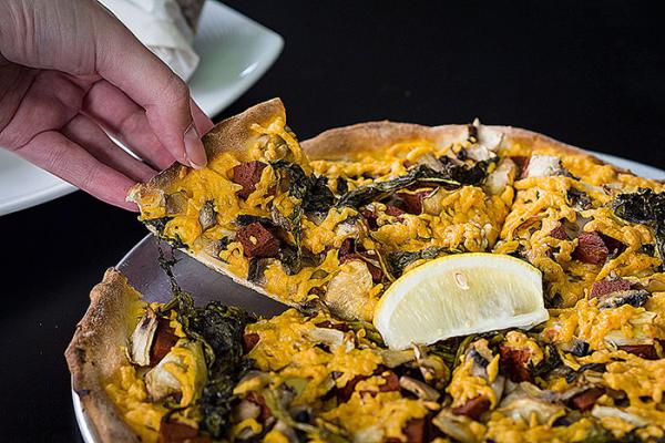 Hand lifting a slice of loaded Lebanese-style pizza topped with chicken, herbs and a lemon wedge