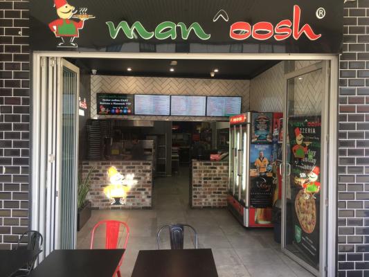 Entrance to a Man'oosh Lebanese pizza takeaway with menu boards and outdoor seating