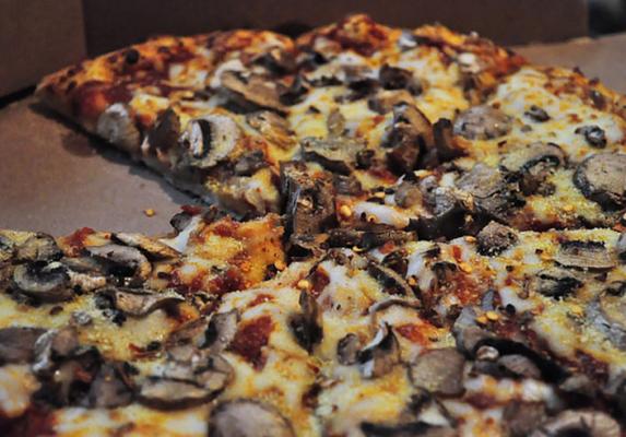 Close-up of sliced mushroom pizza with melted cheese in a cardboard takeaway box