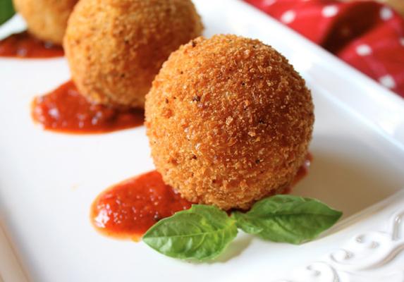 Two golden crumbed savoury balls with red dipping sauce and fresh basil on a white plate