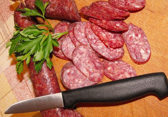 Sliced spicy salami with parsley and a kitchen knife on a wooden chopping board