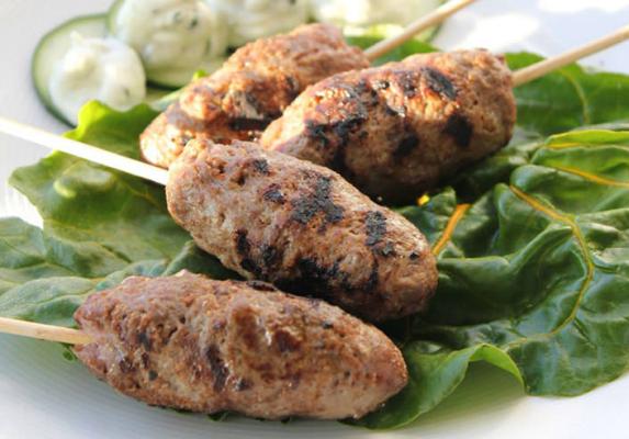 Grilled lamb kafta skewers on leafy greens with cucumber slices