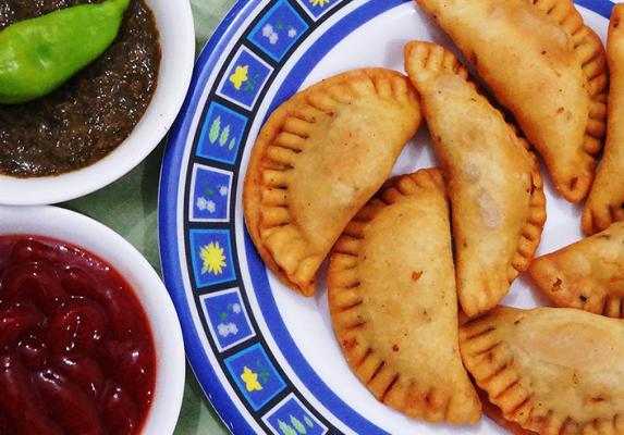 Golden fried Lebanese sambousek pastries on a patterned plate with chilli and dipping sauces