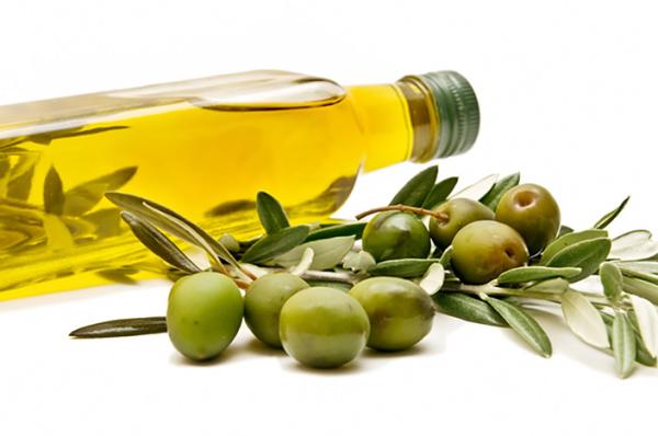 Bottle of olive oil beside fresh green olives and olive leaves on a white background