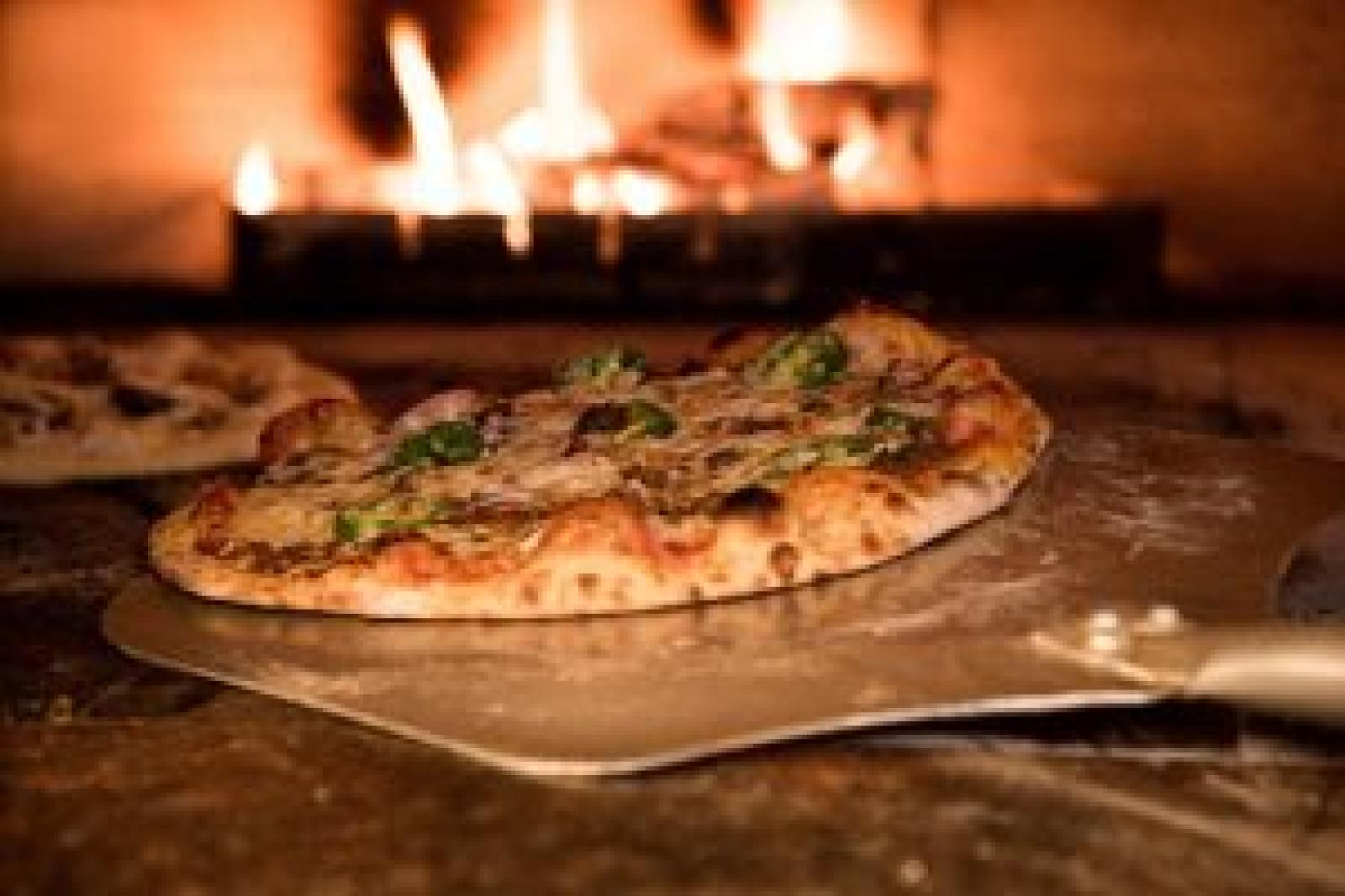 Freshly baked Lebanese manoosh on a pizza peel in front of a wood-fired oven