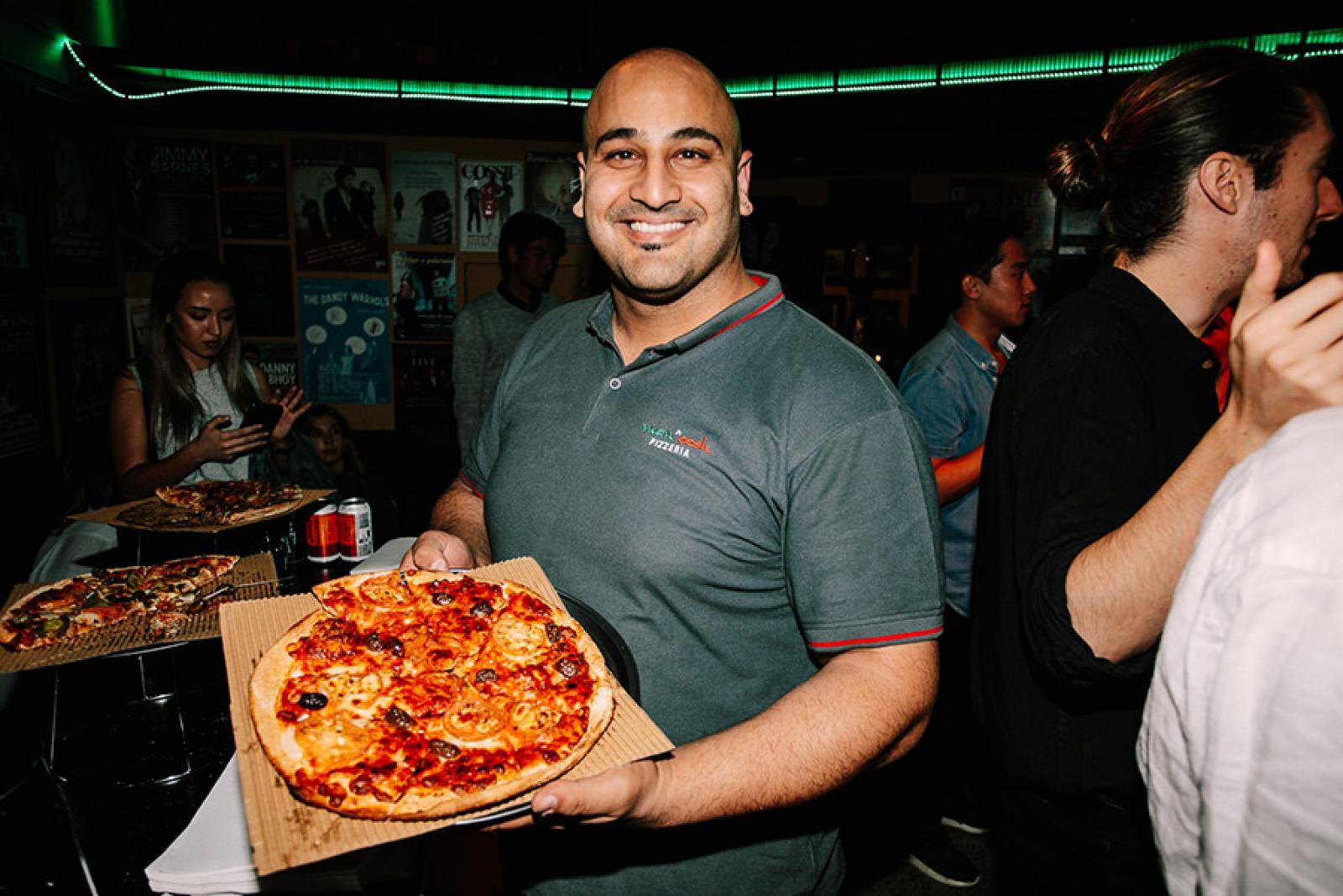 Smiling man holding a freshly baked pepperoni pizza at a lively restaurant event