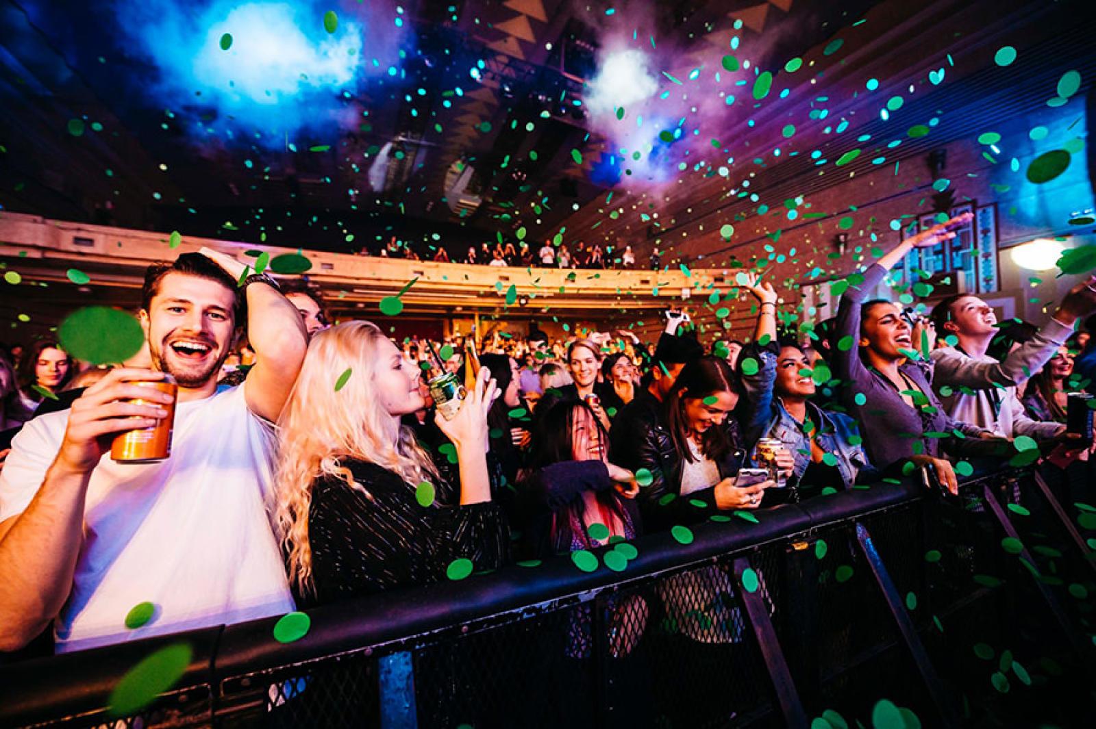 Smiling concert crowd enjoying a live music event under colourful stage lights