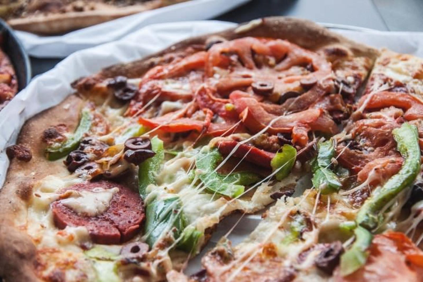 Close-up of a sliced loaded pizza with melted cheese, capsicum, olives and savoury toppings