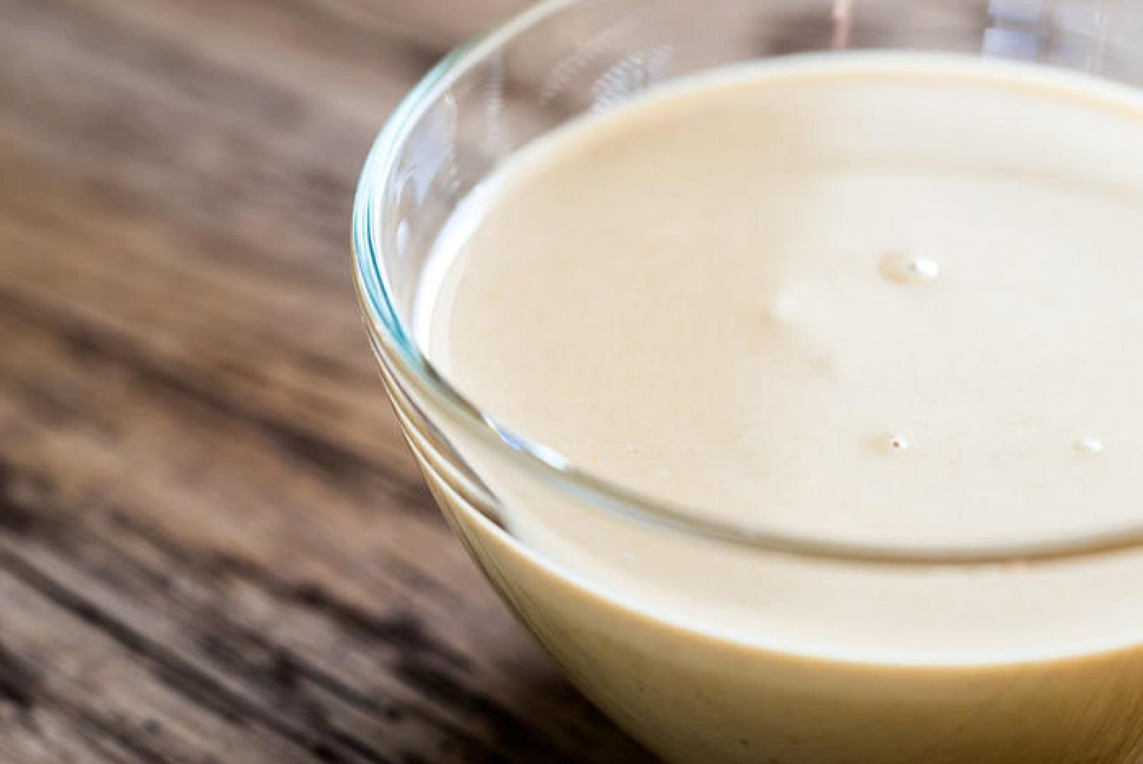 Small glass bowl of smooth creamy tahini sauce on a rustic wooden table
