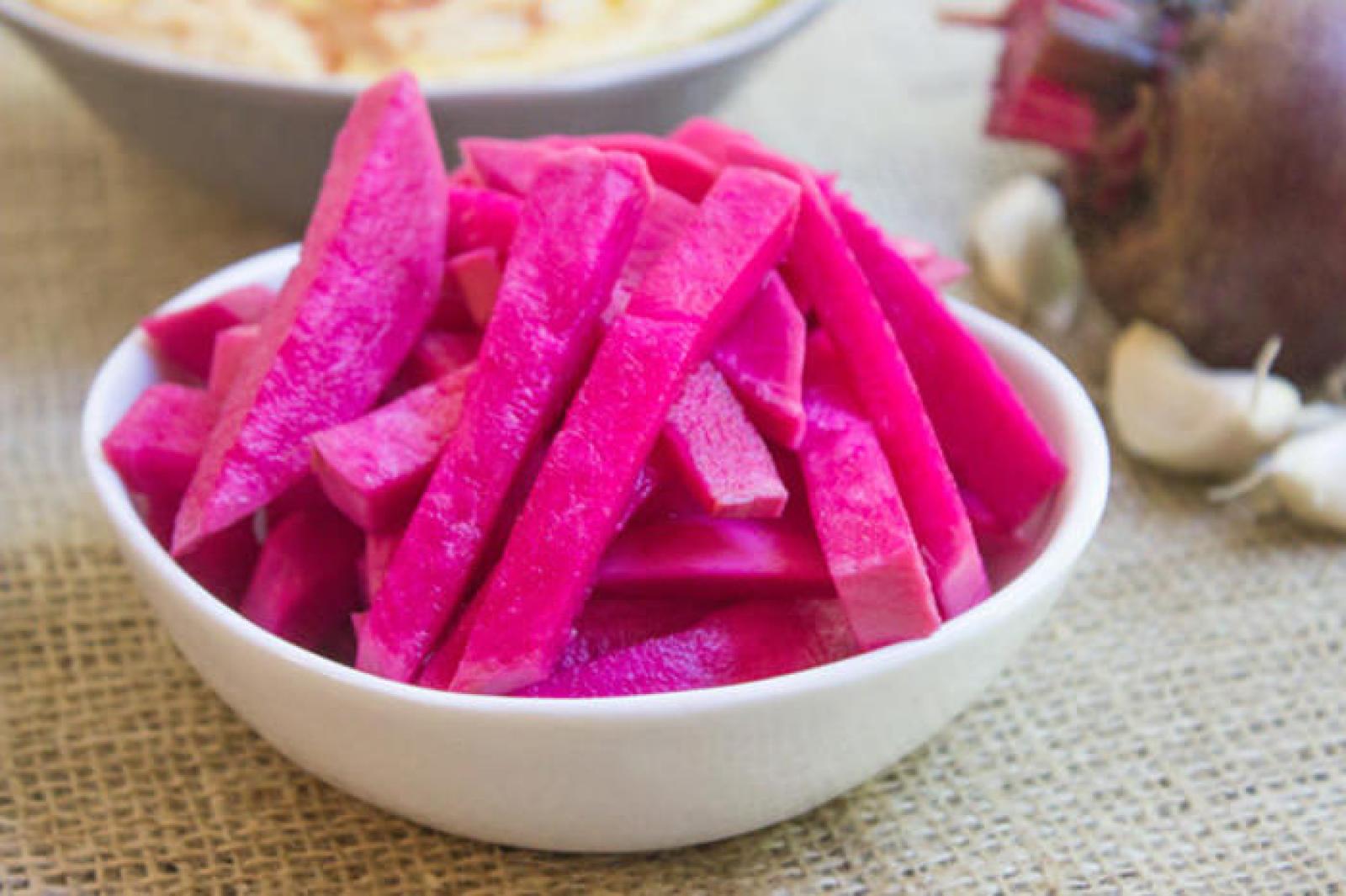 White bowl filled with bright pink pickled turnip batons on a rustic table