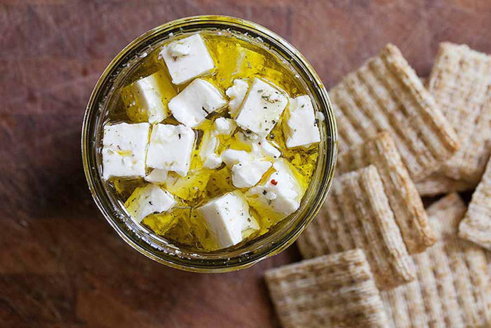 Bowl of feta cheese cubes in olive oil with herbs, served beside crisp crackers