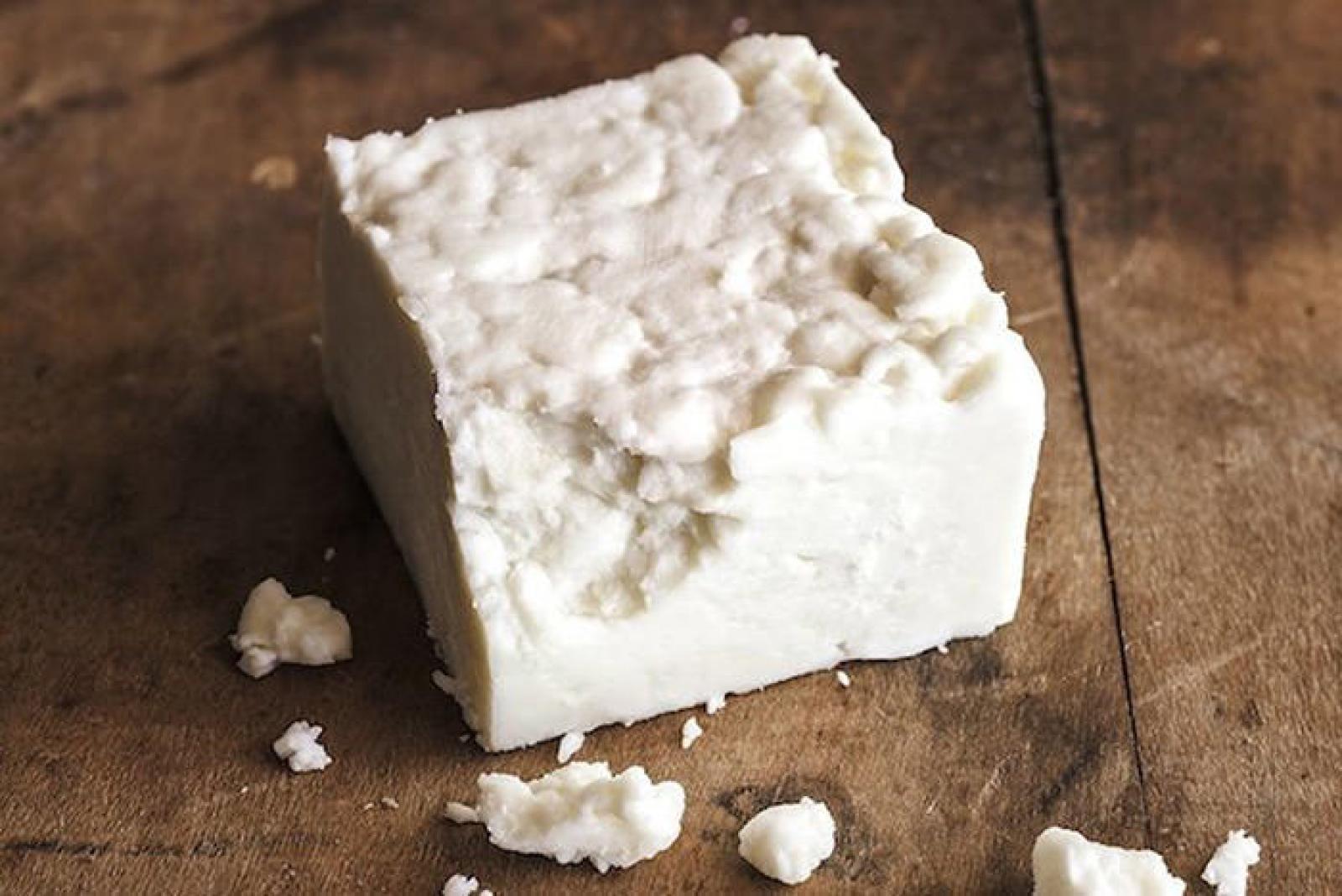 Block of crumbly feta cheese on a rustic wooden board with scattered cheese pieces