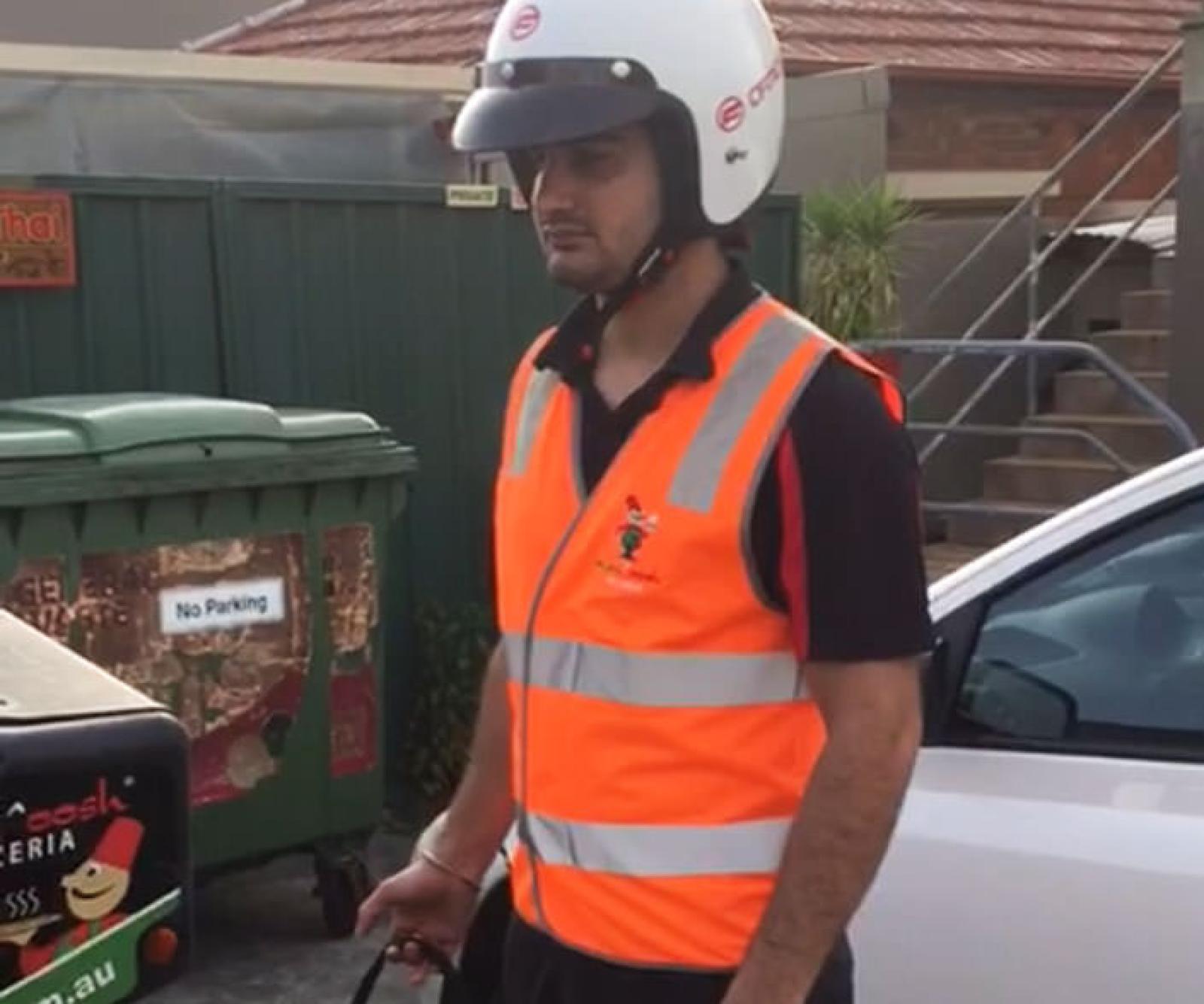OOSHMAN delivery driver in helmet and high-visibility vest beside a car