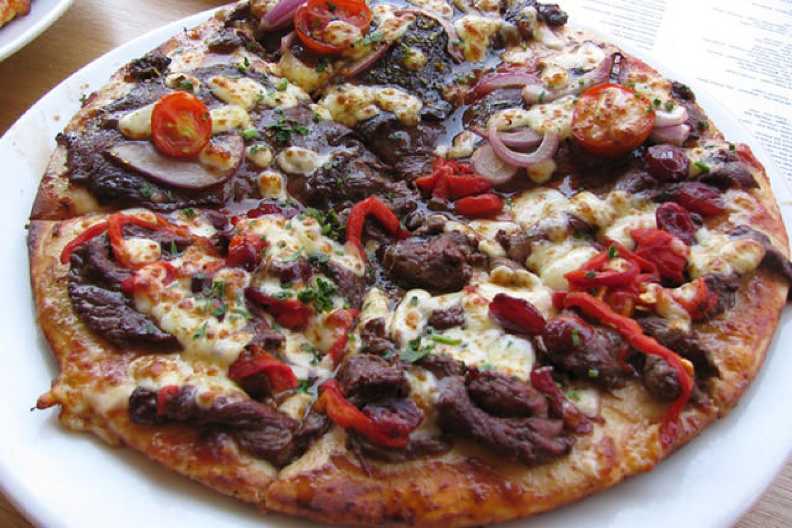 Loaded pizza topped with olives, red onion, cherry tomatoes, capsicum and melted cheese