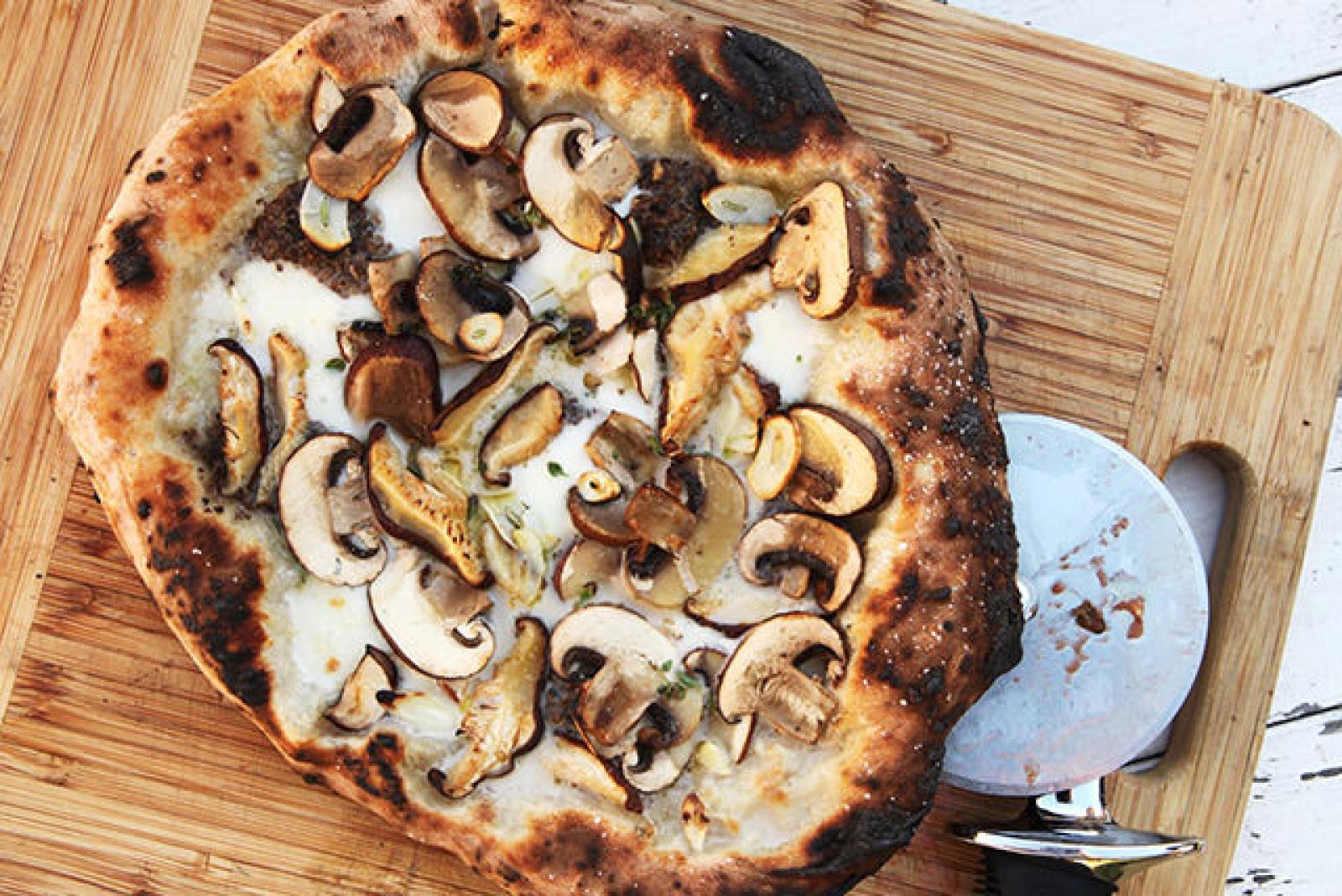 Wood-fired mushroom pizza with melted cheese on a wooden board