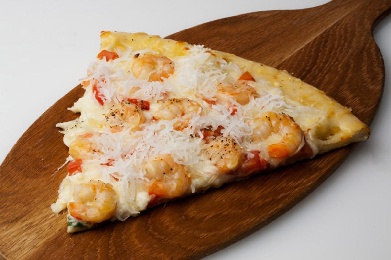 Cheesy prawn pizza slice with tomato on a wooden serving board