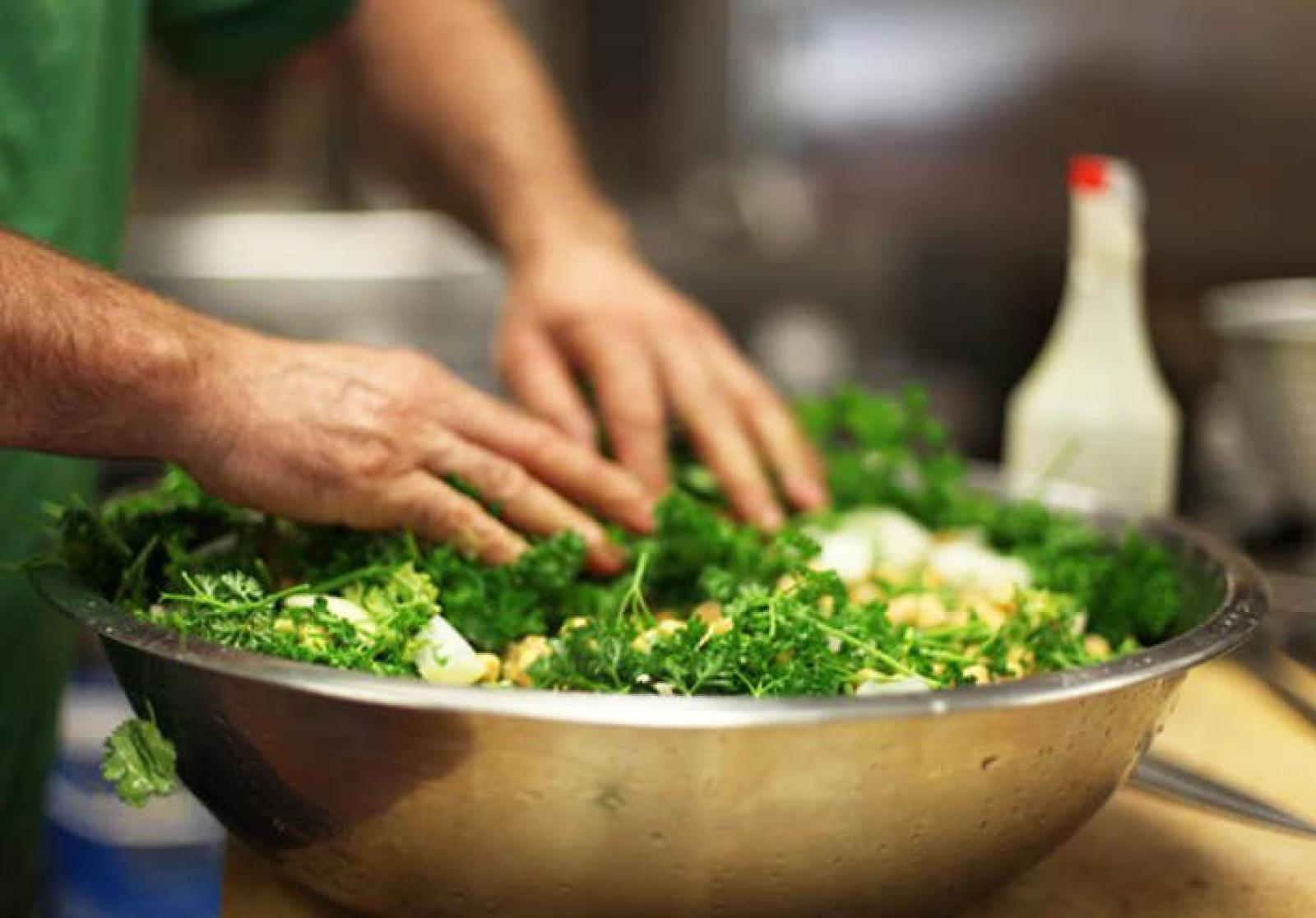 Chef mixing fresh tabouli salad with herbs and chopped vegetables in a large bowl