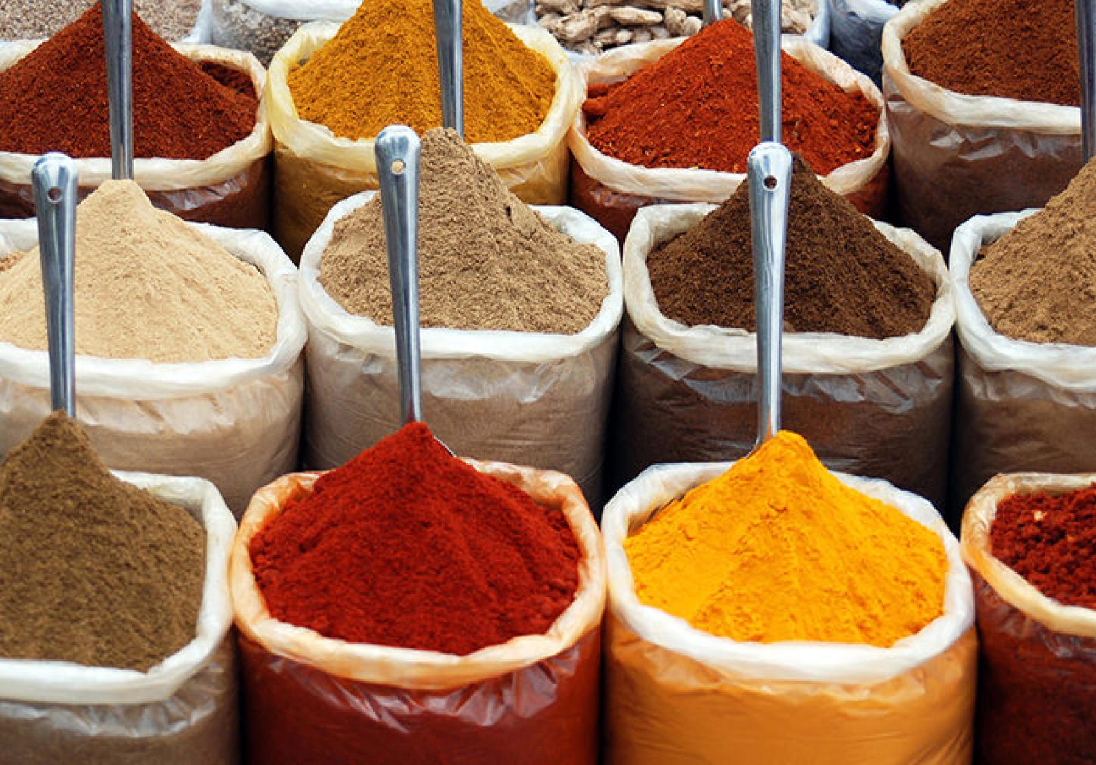 Open sacks of colourful ground spices with metal scoops at a market stall