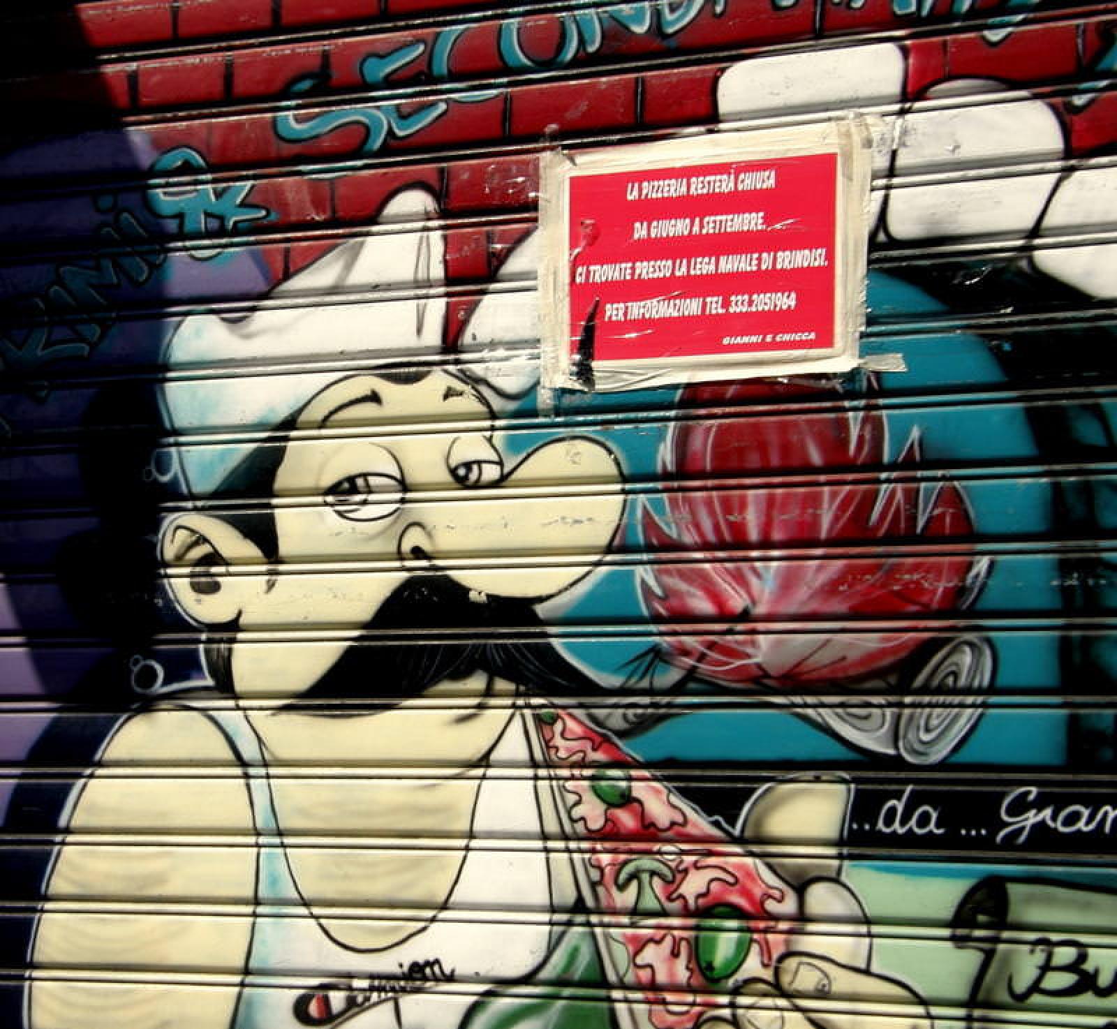 Colourful street-art mural of a chef holding a pizza on an OOSHMAN shopfront shutter