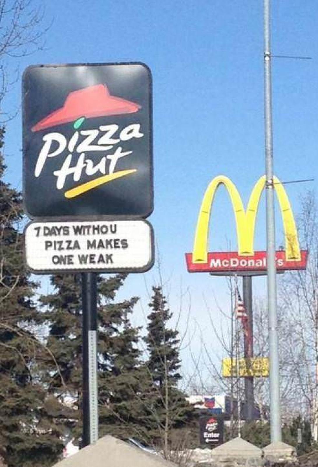 Pizza Hut roadside sign reading ‘7 days without pizza makes one weak’ beside McDonald’s golden arches