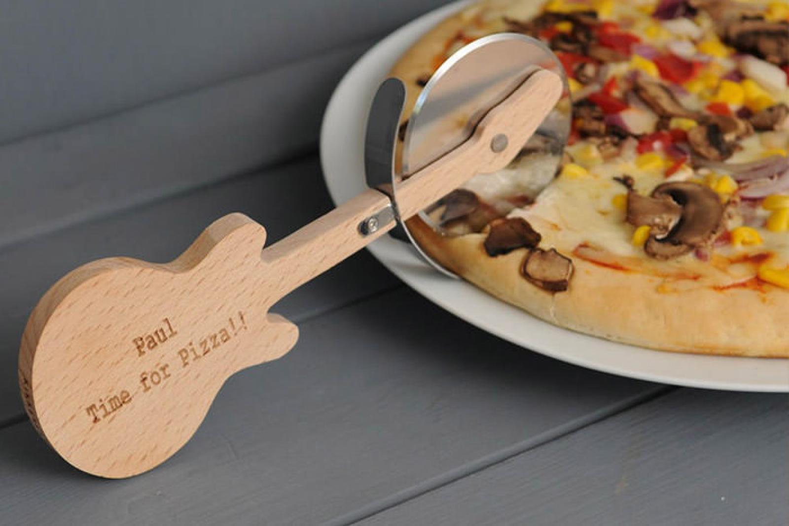 Wooden guitar-shaped pizza cutter beside a plate of vegetable pizza on a grey table