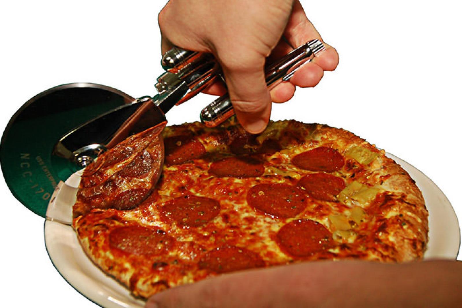 Hand slicing a pepperoni pizza on a white plate with a pizza cutter