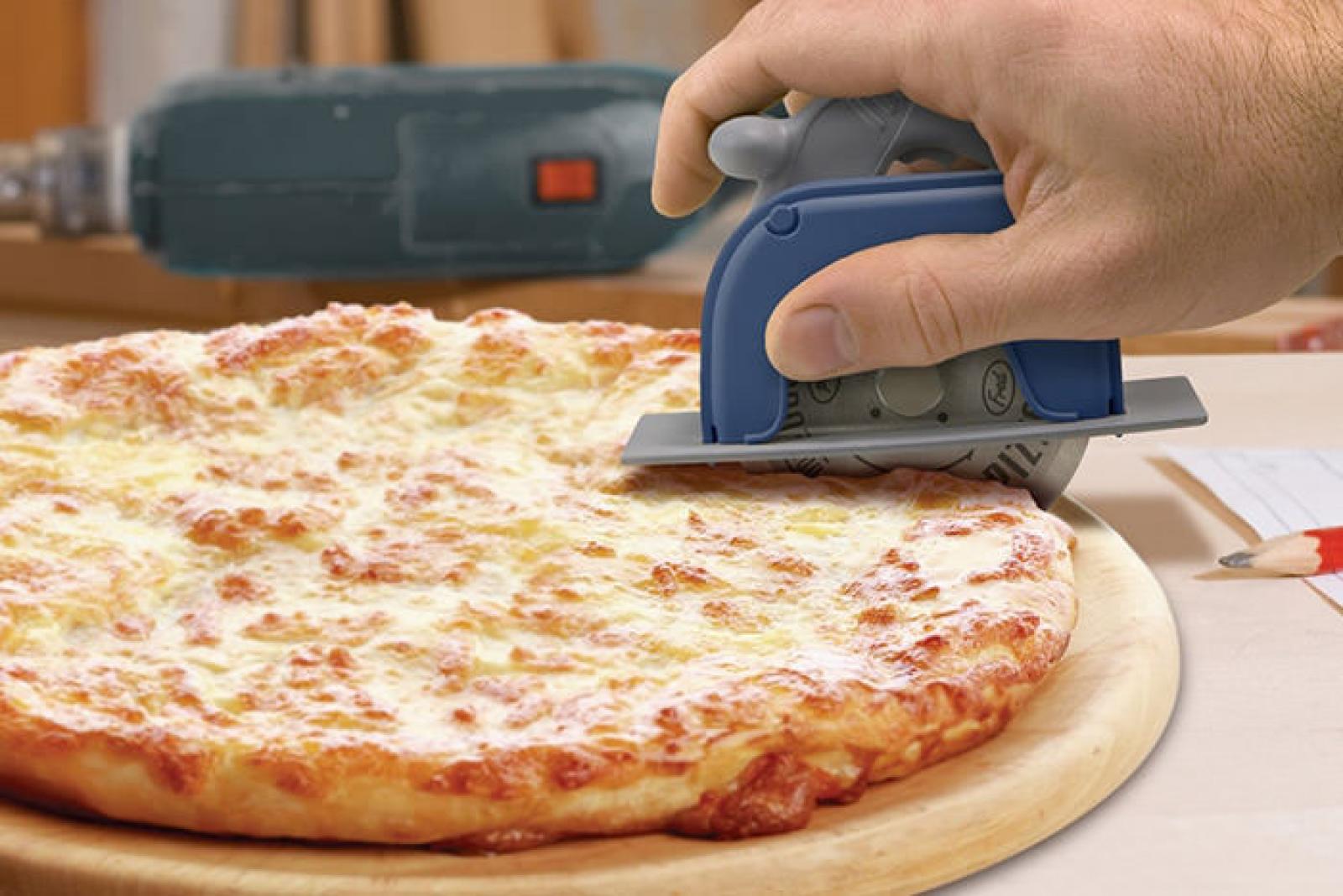 Person using a blue handheld power tool to cut a large cheese pizza on a wooden board