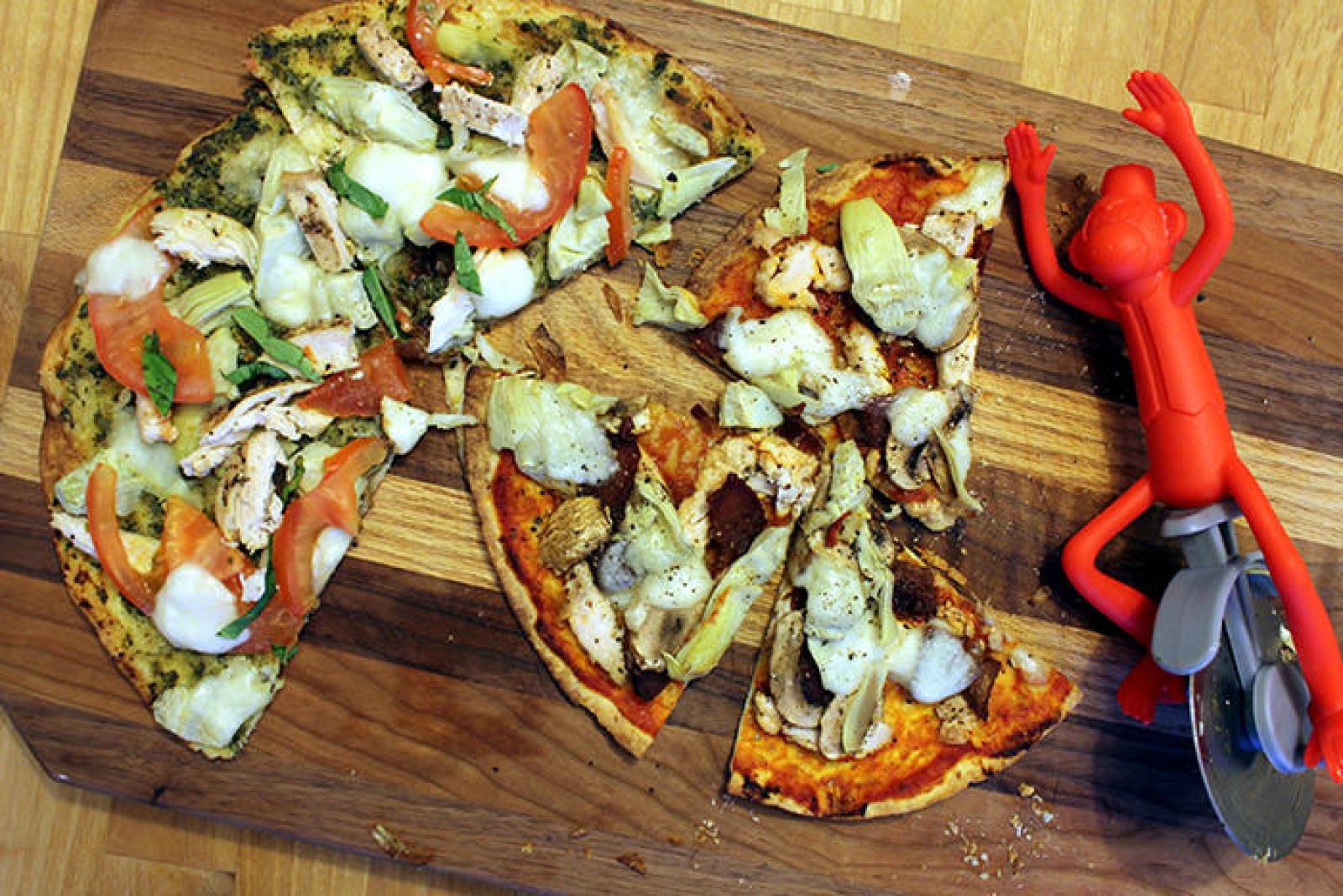 Sliced gourmet pizza with mixed toppings on a wooden board beside a red pizza cutter