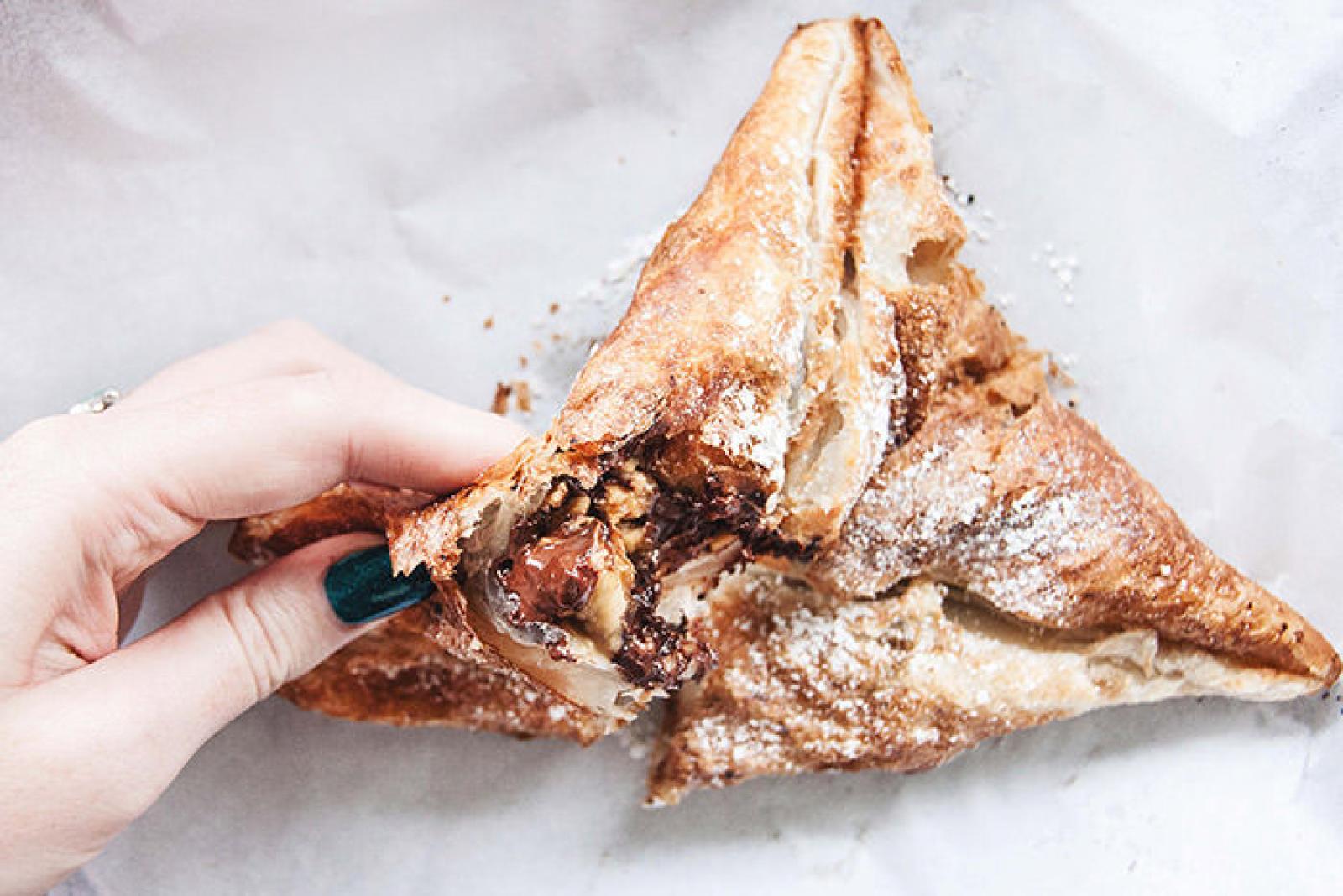 Hand holding a chocolate-filled triangular Lebanese dessert pastry dusted with icing sugar