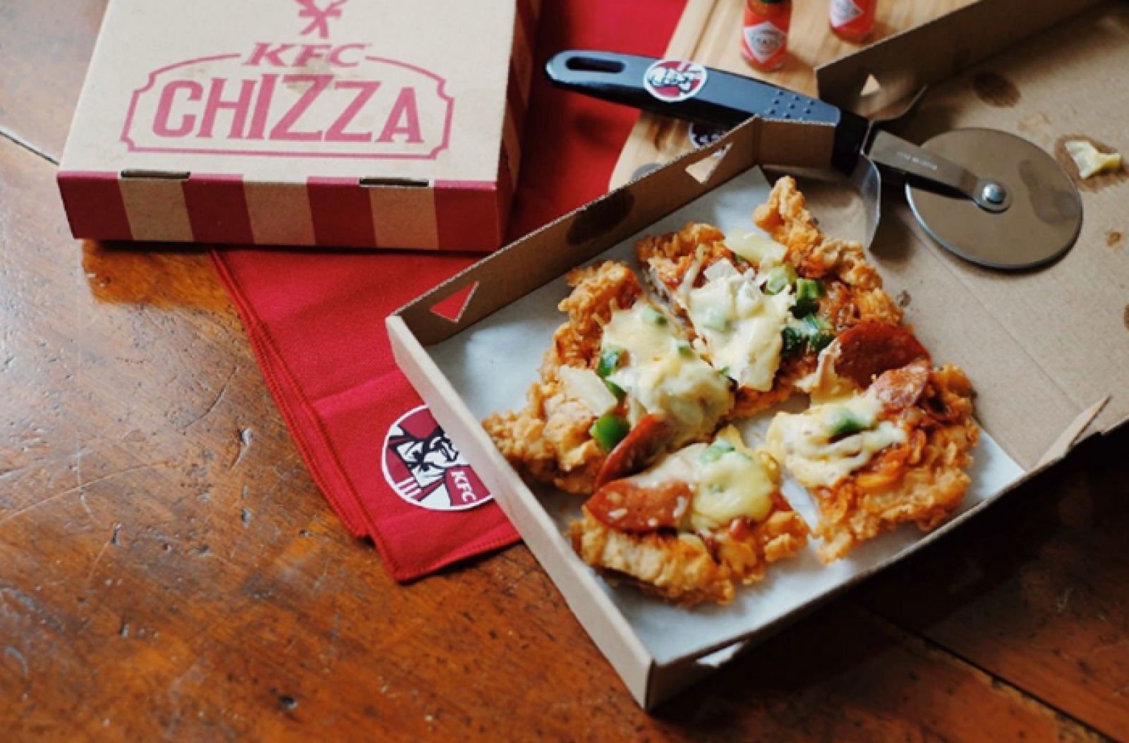 KFC Chizza meal in an open box with a pizza cutter on a wooden table