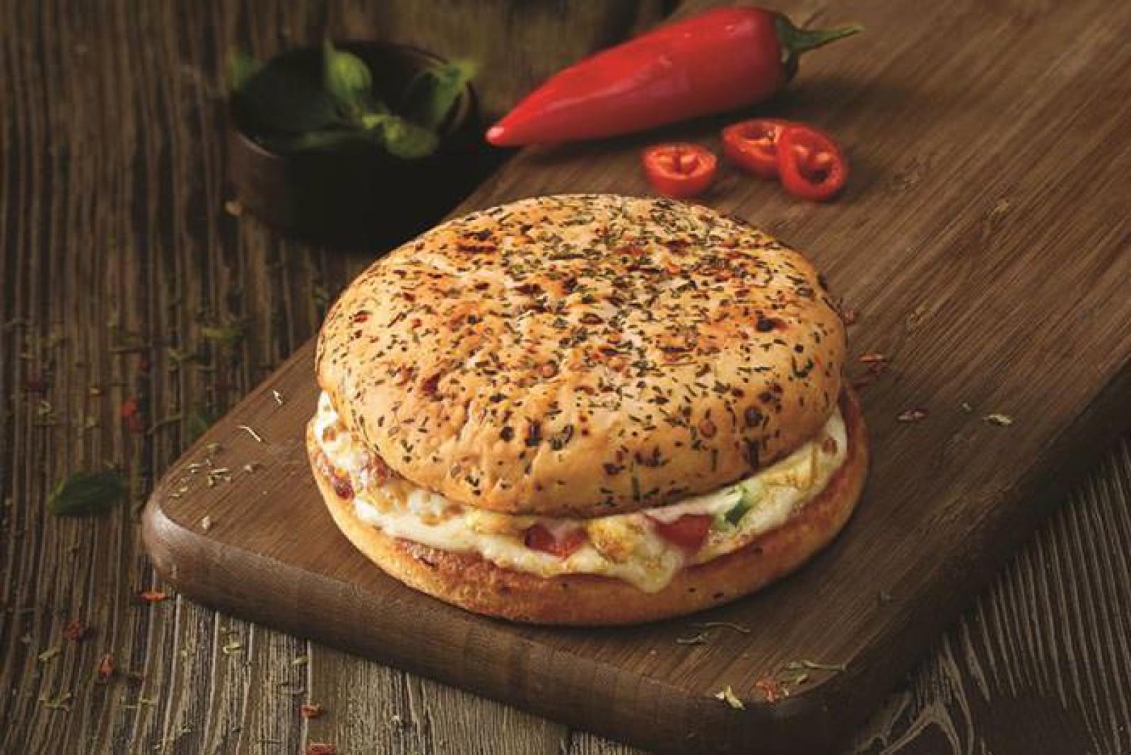 Seeded breakfast roll filled with egg, cheese and sliced tomato on a rustic wooden board