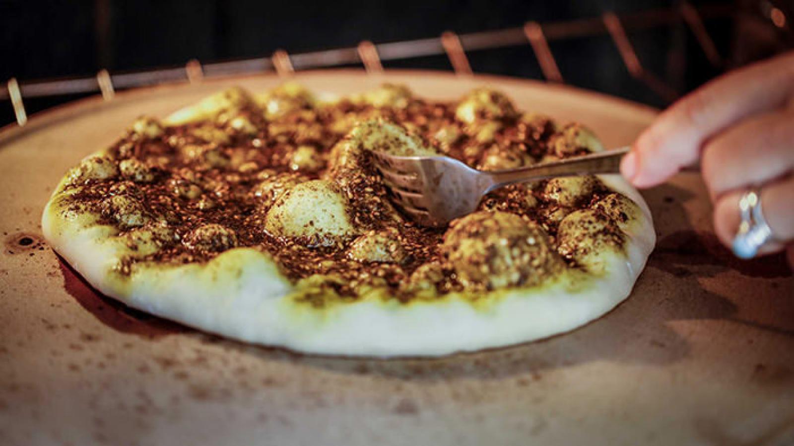 Fresh zaatar manoosh topped with herbs and sesame seeds being sliced