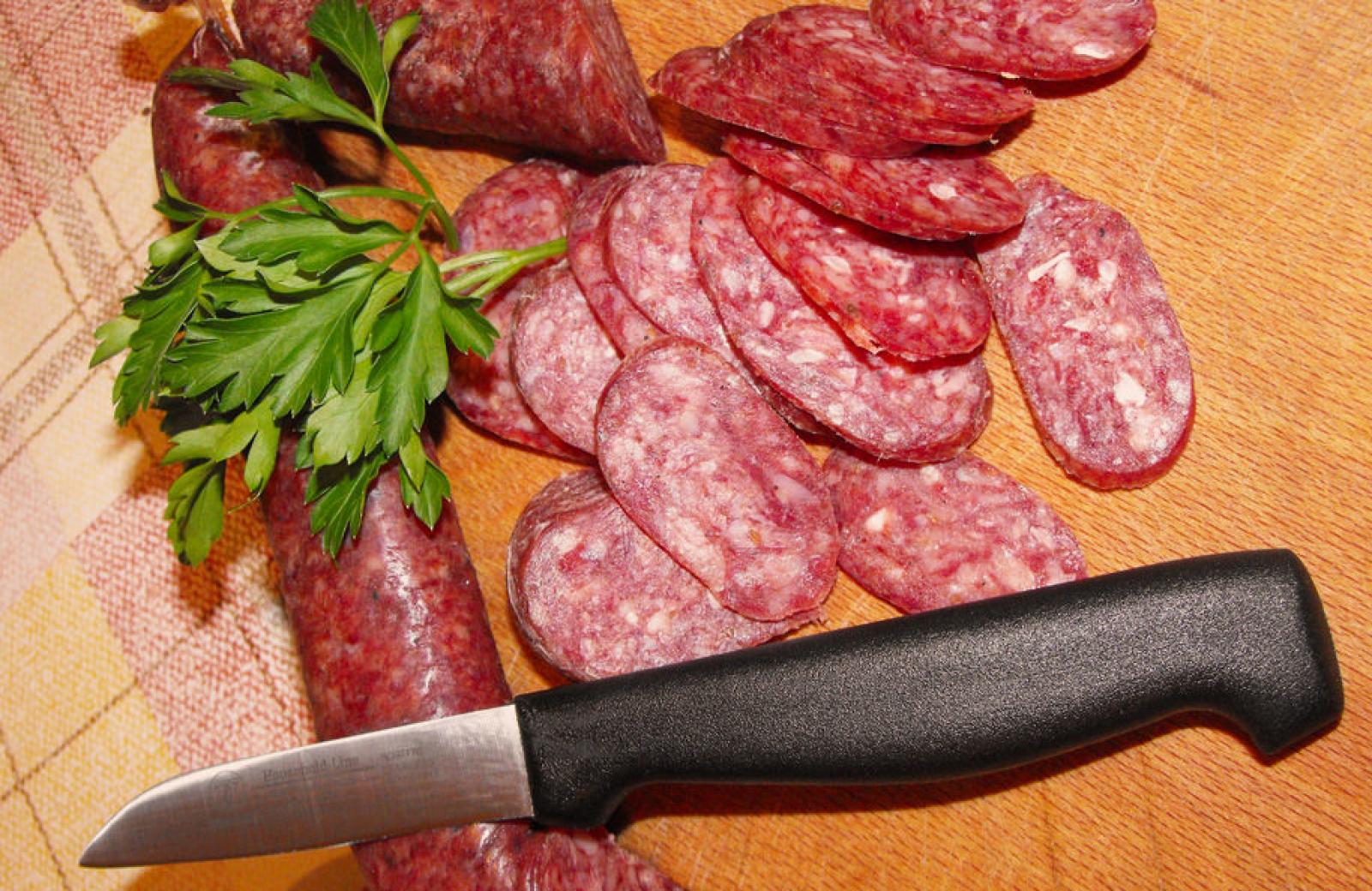 Sliced cured sausage with parsley and a kitchen knife on a wooden board