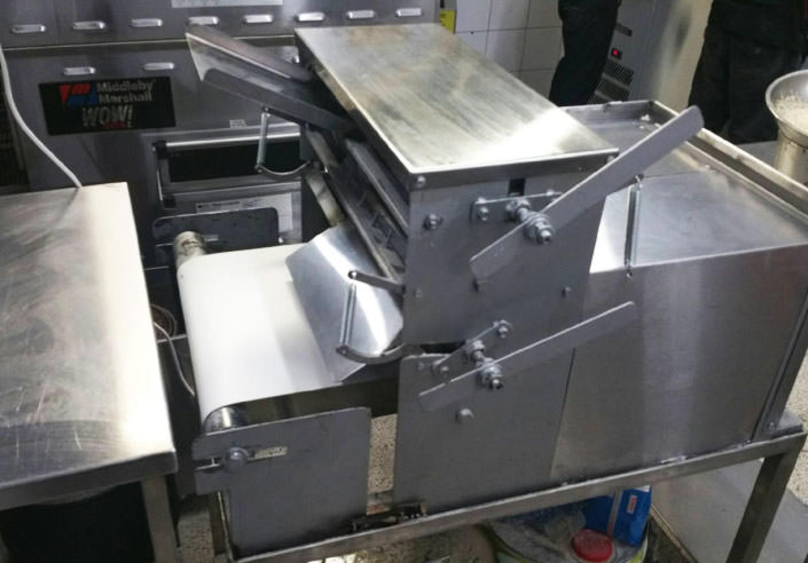 Stainless steel dough roller machine used to prepare fresh pizza dough in a commercial kitchen