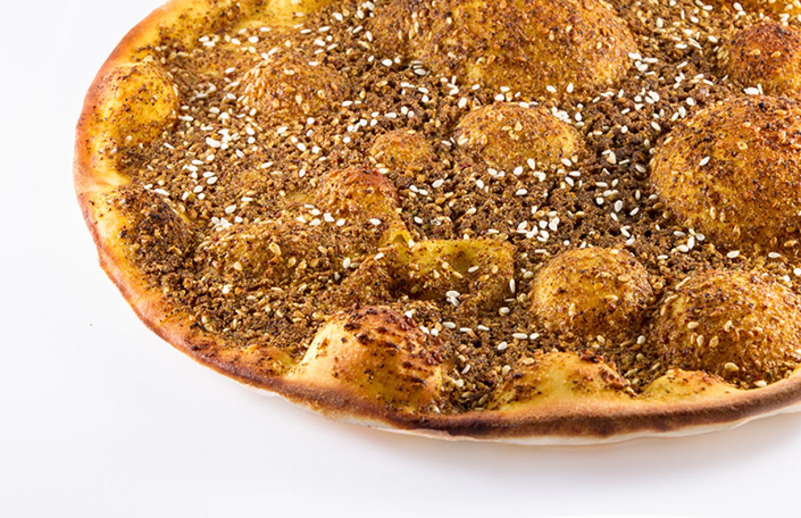 Close-up of a golden Lebanese zaatar manoosh topped with aromatic herb and sesame blend