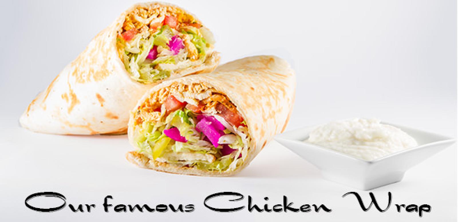 Two halves of a chicken wrap with fresh salad filling beside a bowl of creamy garlic dip