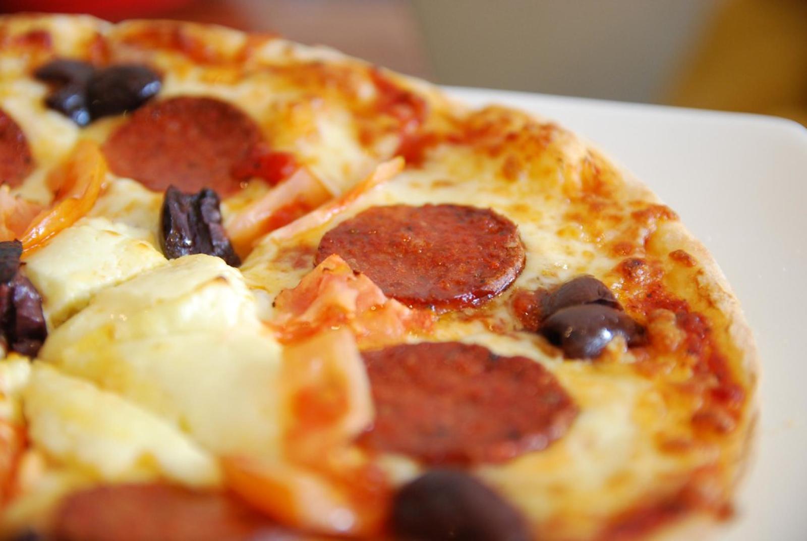 Close-up of a pepperoni pizza with melted cheese, black olives and feta on a white plate