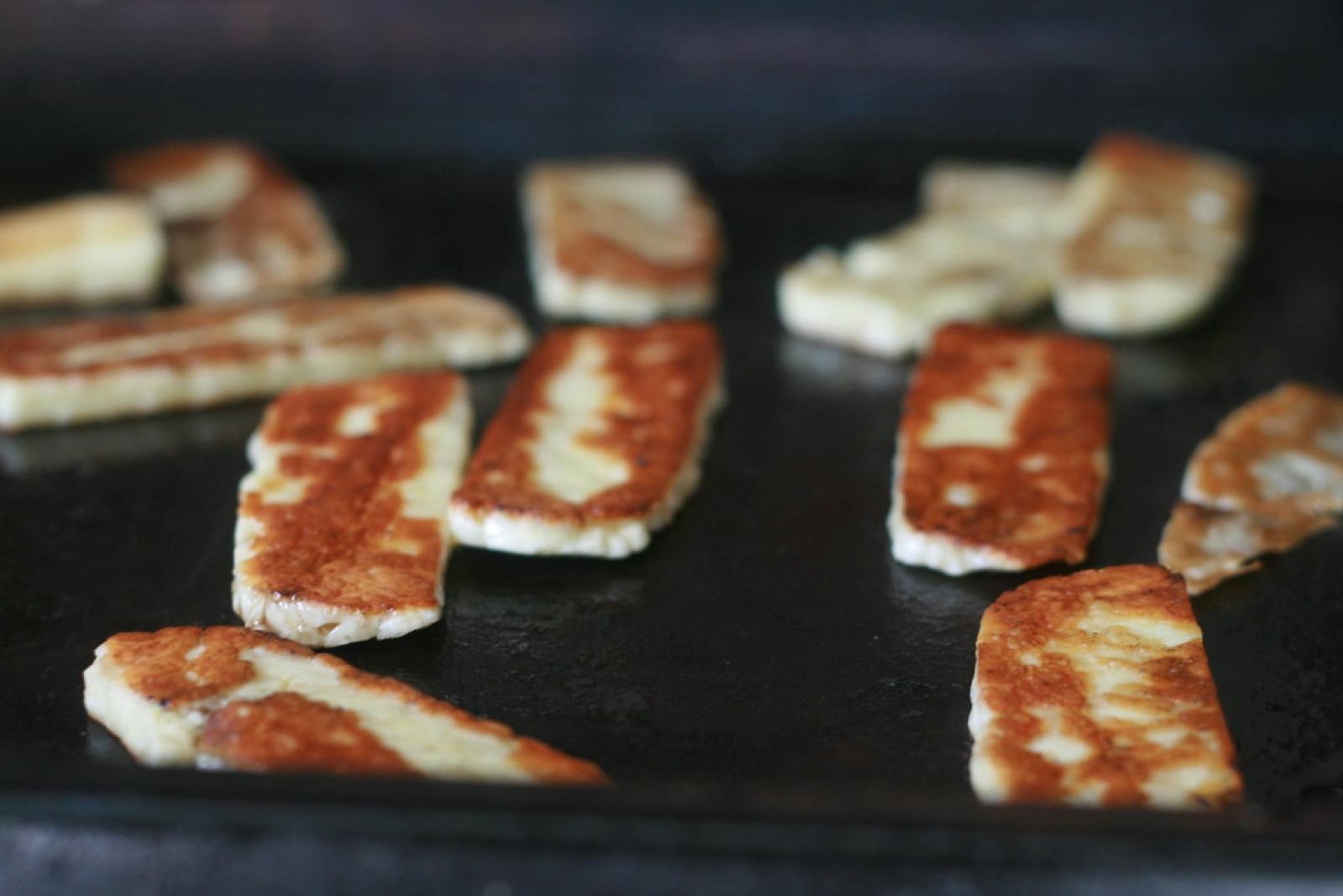 Slices of haloumi cheese grilling on a hot flat-top plate