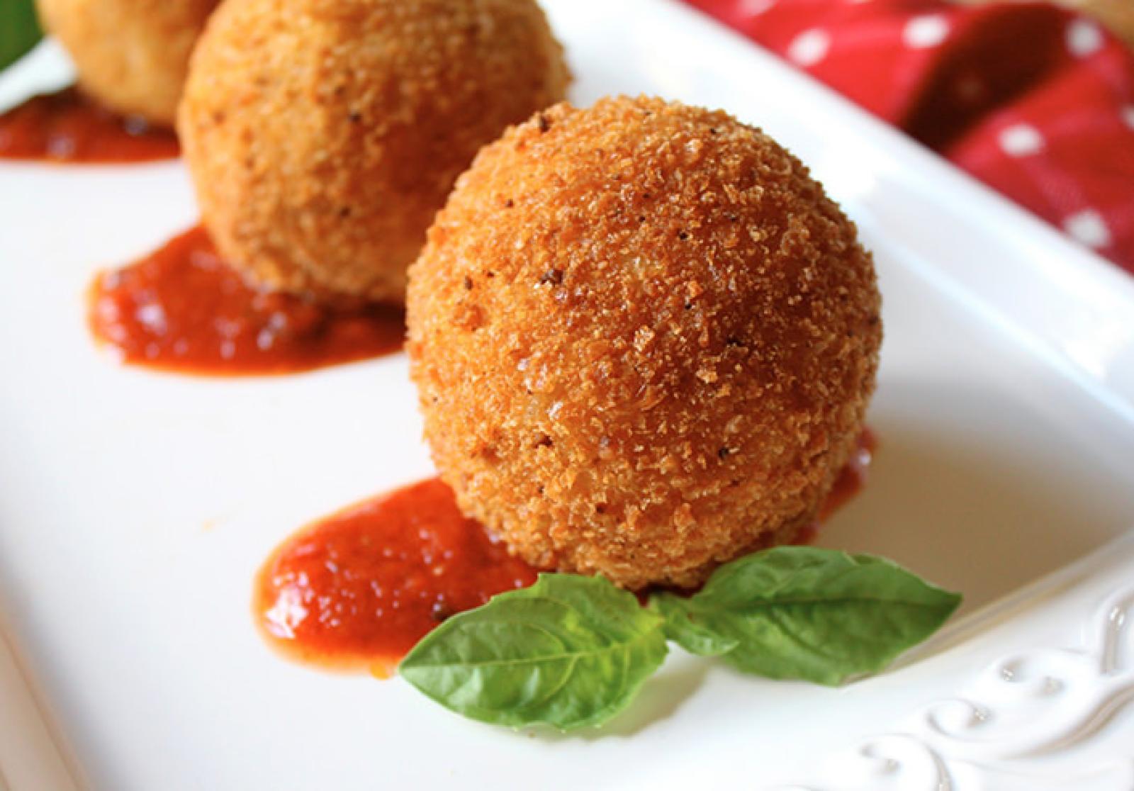 Three golden crumbed cheese balls with tomato dipping sauce and fresh basil