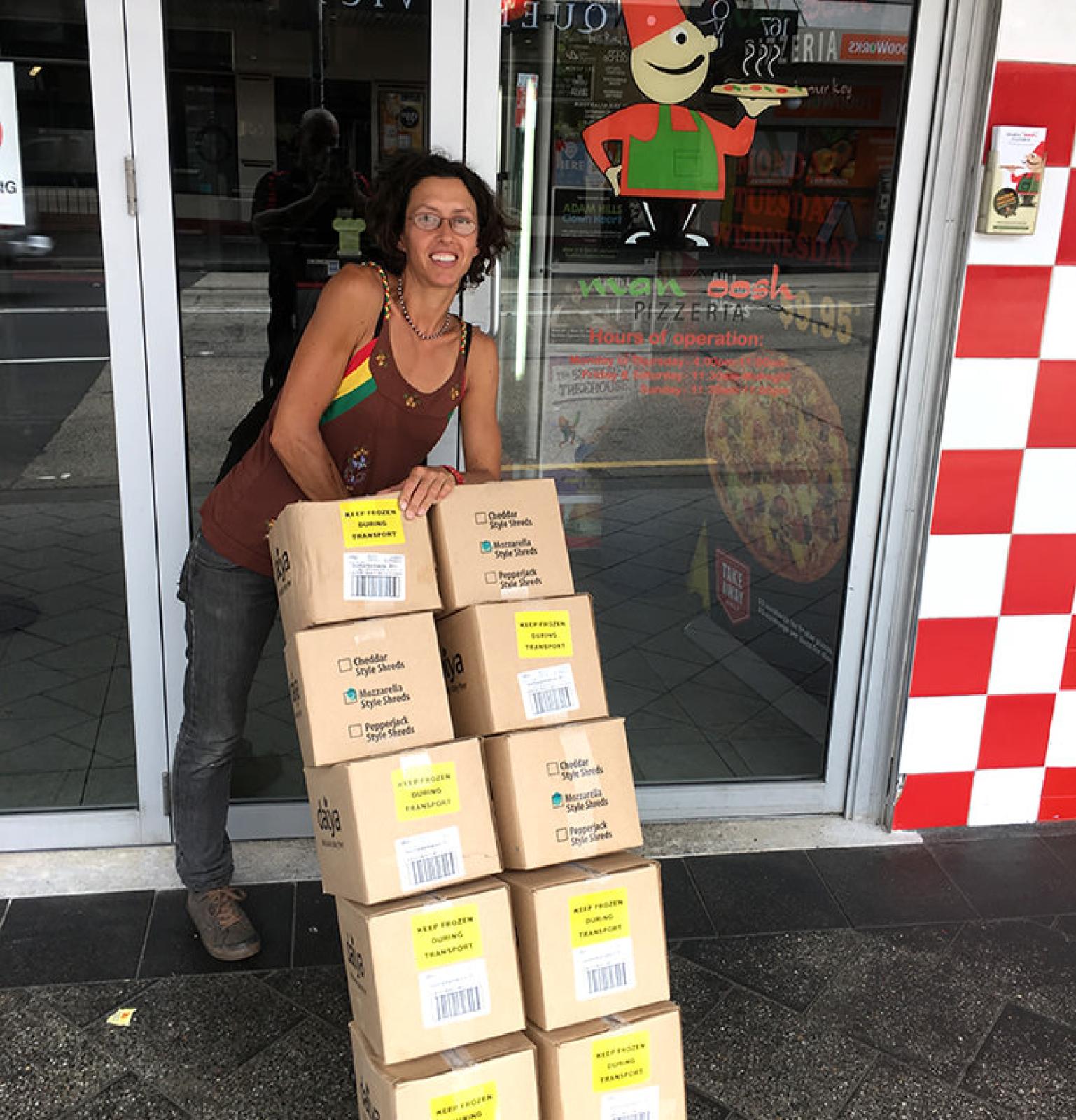 OOSHMAN team member beside stacked delivery boxes outside a restaurant entrance